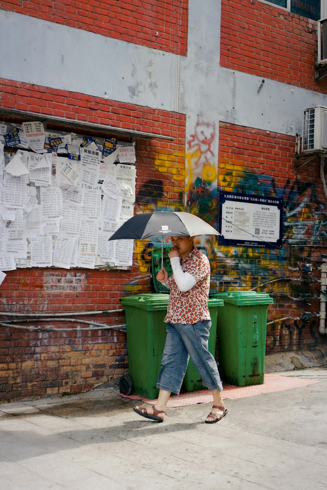 woman in green and yellow floral dress holding umbrella standing beside wall with graffiti