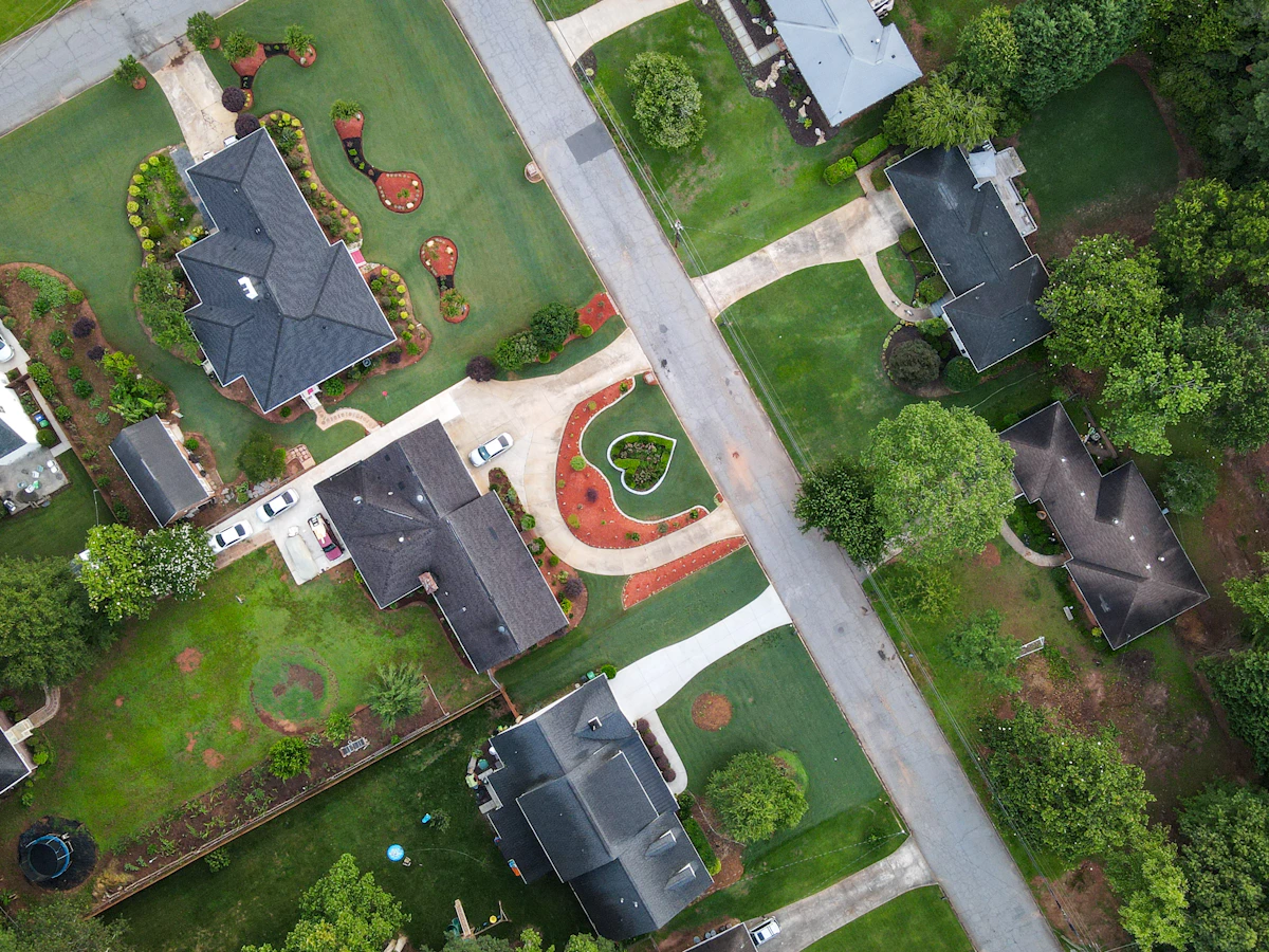 Aerial view of a leafy suburban street with manicured lawns, mulched beds, and homes along a neighborhood route