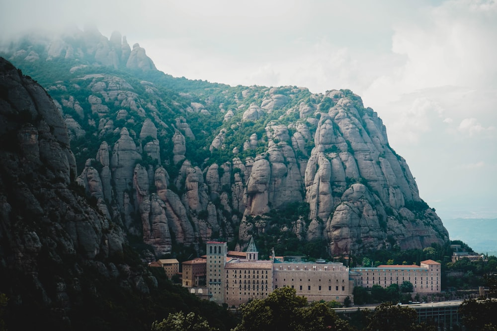 Edificio de hormigón blanco cerca de la montaña rocosa gris bajo nubes blancas durante el día