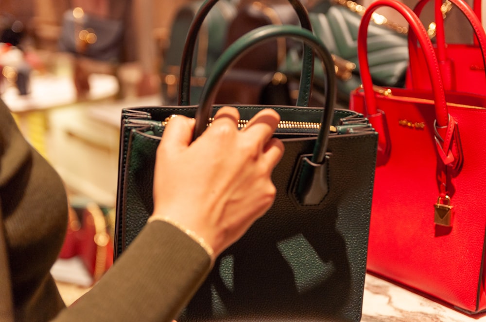 person holding black leather handbag