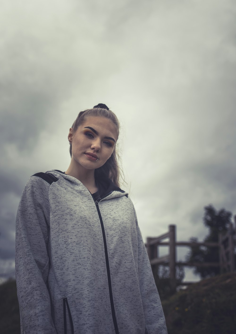 woman in gray hoodie standing near brown wooden fence during daytime