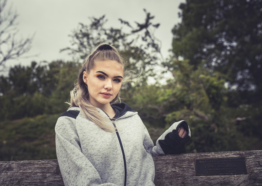 girl in gray hoodie standing on brown wooden fence during daytime