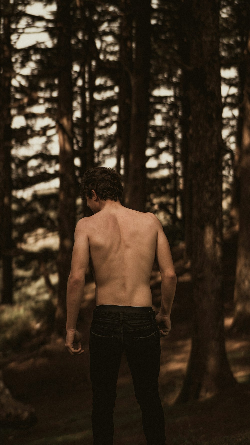 topless man in black shorts standing in forest