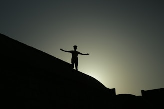A silhouette of a man standing on a hilltop with arms raised at dawn