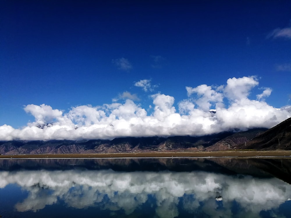 body of water near mountain under blue sky and white clouds during daytime