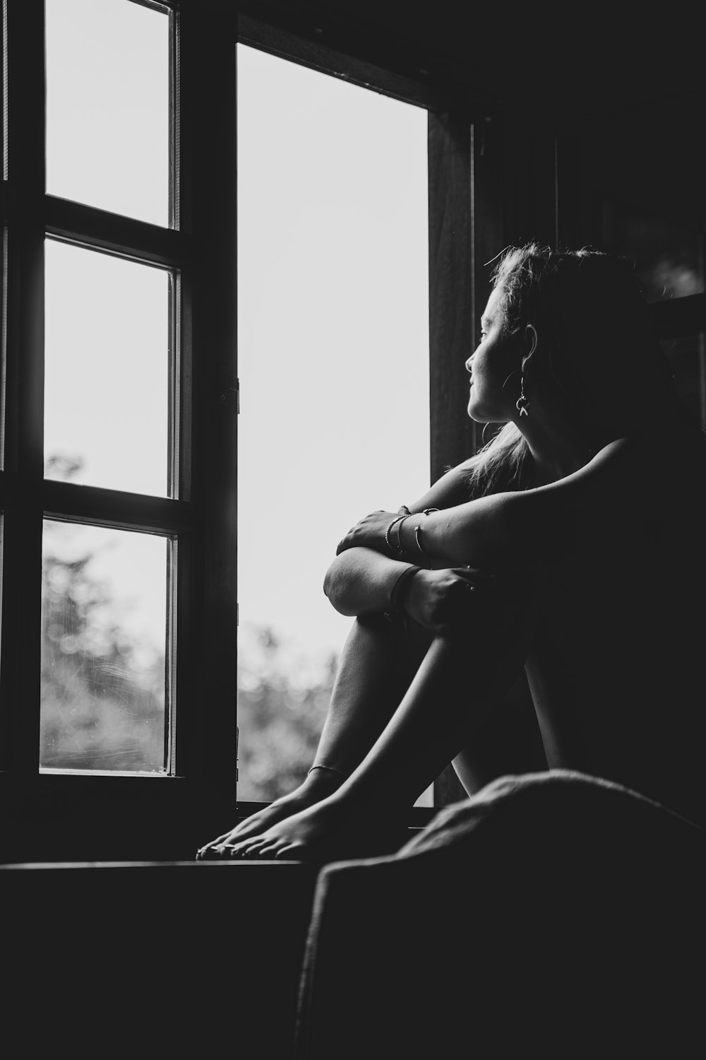 grayscale photo of woman sitting on window