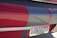 A close-up of a car's rear featuring a personalized license plate with the text 'GUILTY'. The vehicle is painted with red and gray colors, and the plate has a pink ribbon design, commonly associated with breast cancer awareness.