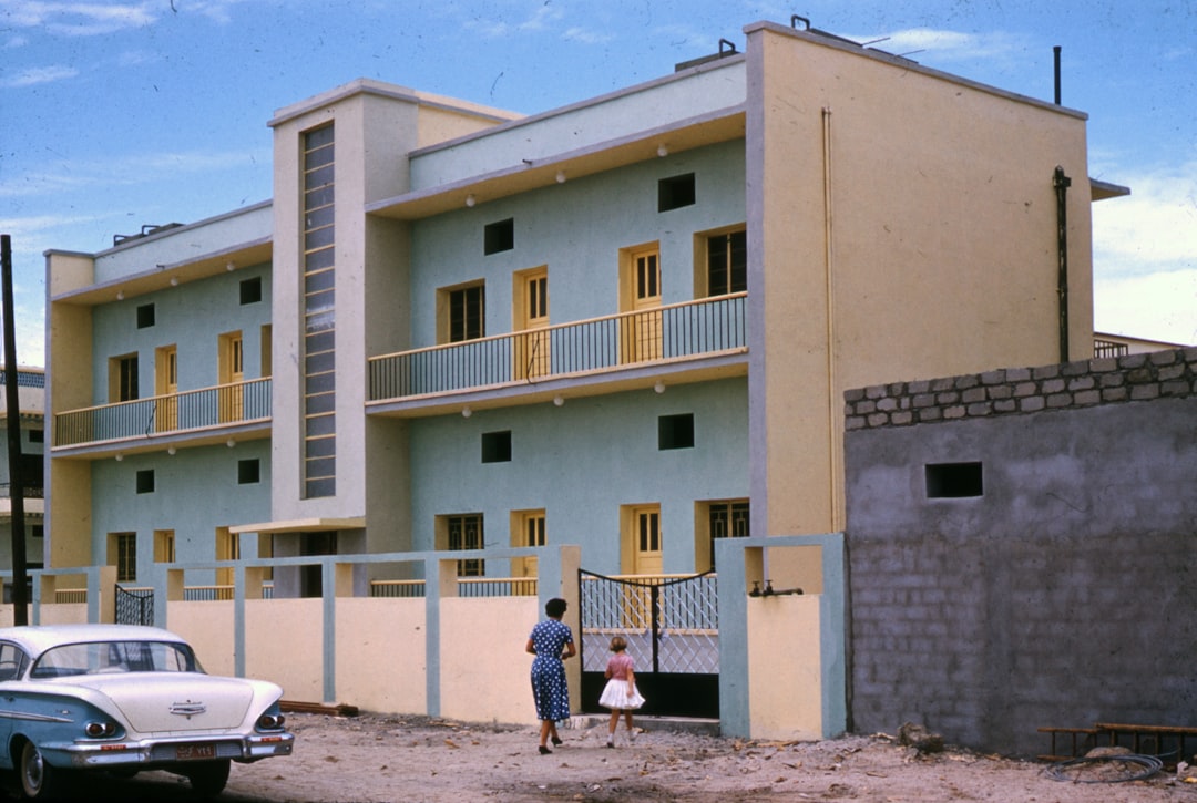 woman in white and black stripe shirt walking on brown sand near white concrete building during