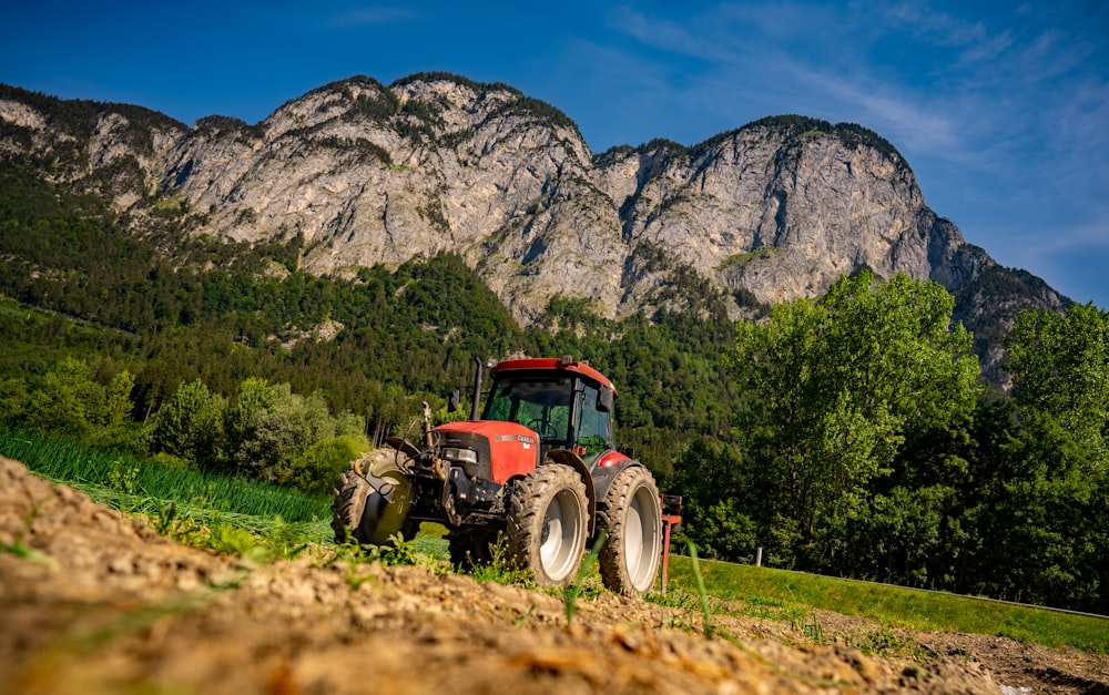 red tractor on green grass field near mountain under blue sky during daytime