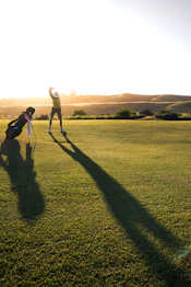 A golfer swinging a club on a green course at low sun