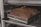 Two loaves of bread are placed in a metal baking pan on an oven rack. The bread has a dark, golden-brown crust, and the pans are labeled 'Chicago Metallic'. The setting appears to be an industrial kitchen or bakery.
