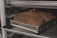 Two loaves of bread are placed in a metal baking pan on an oven rack. The bread has a dark, golden-brown crust, and the pans are labeled 'Chicago Metallic'. The setting appears to be an industrial kitchen or bakery.