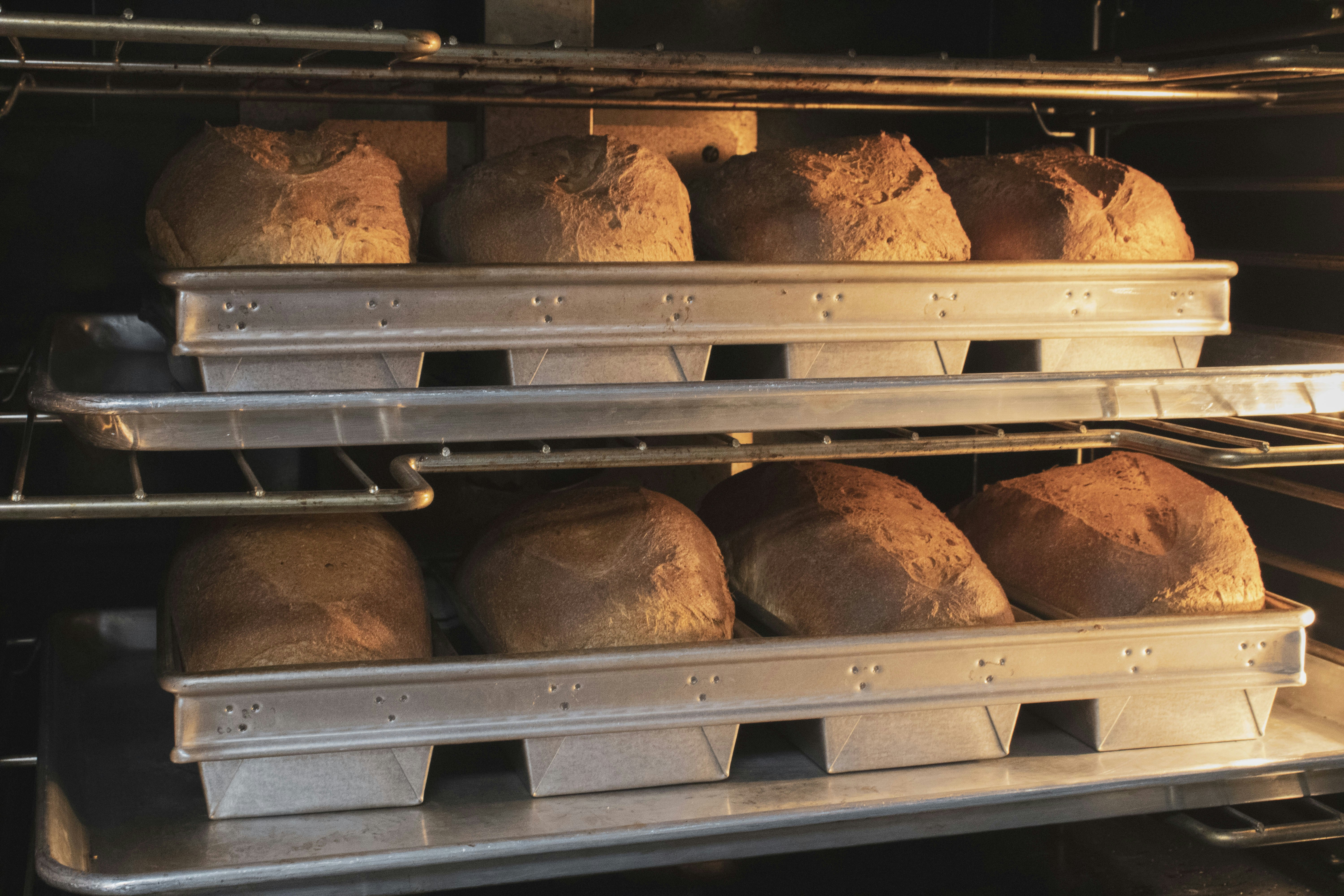 Golden bread loaves inside a professional bakery oven, deep amber tones, oven glow, artisan baking process