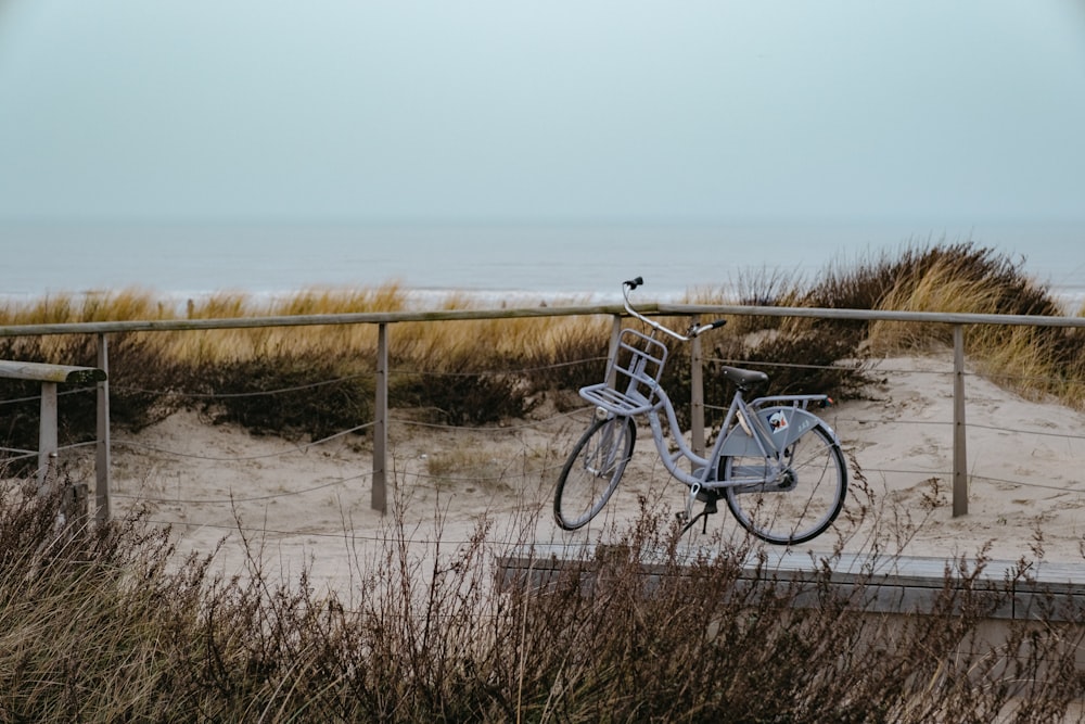 Bicicleta azul y blanca en arena marrón cerca del mar durante el día