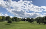Golfers teeing off on a lush green course near the coastline under a bright sky.