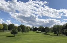 Golfers teeing off on a lush green course near the coastline under a bright sky.