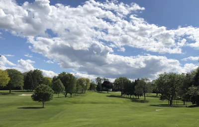 A panoramic view of a lush green golf course under a clear blue sky, with players teeing off in the distance.