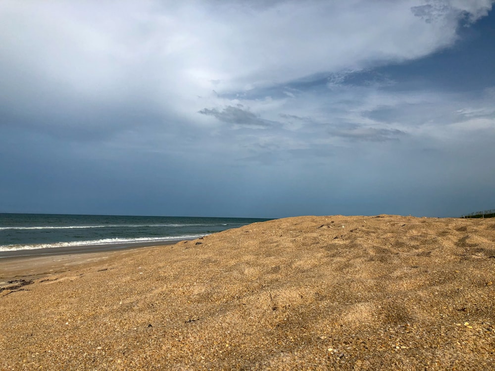 brown sand near body of water under white clouds during daytime