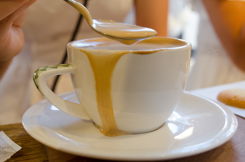 weiße Keramiktasse mit Edelstahllöffel auf weißer Keramikuntertasse