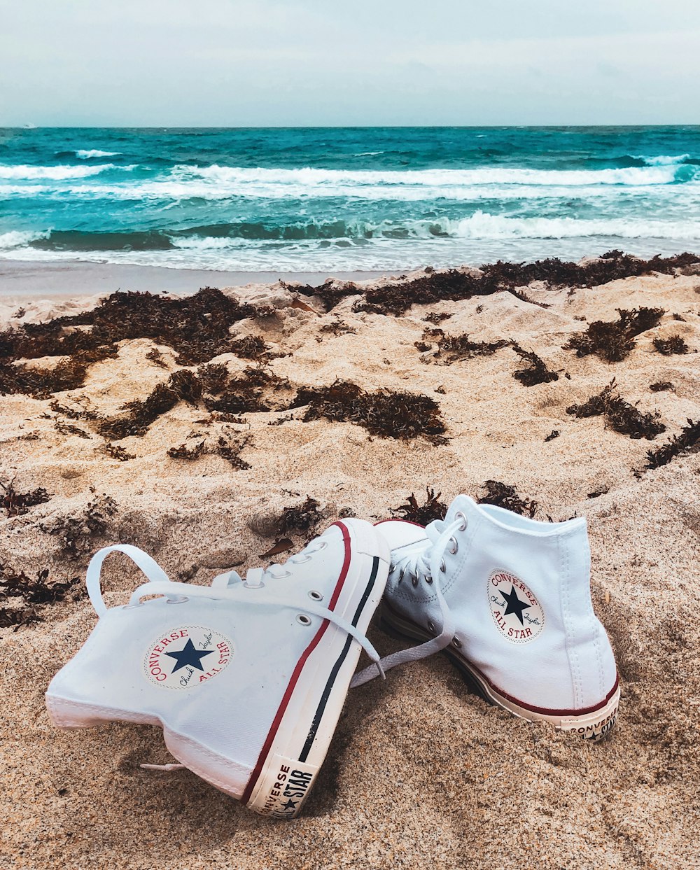 white converse all star high top sneakers on beach shore