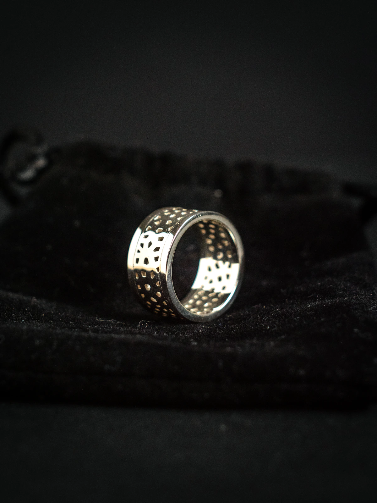 A patterned silver ring resting on folded black fabric