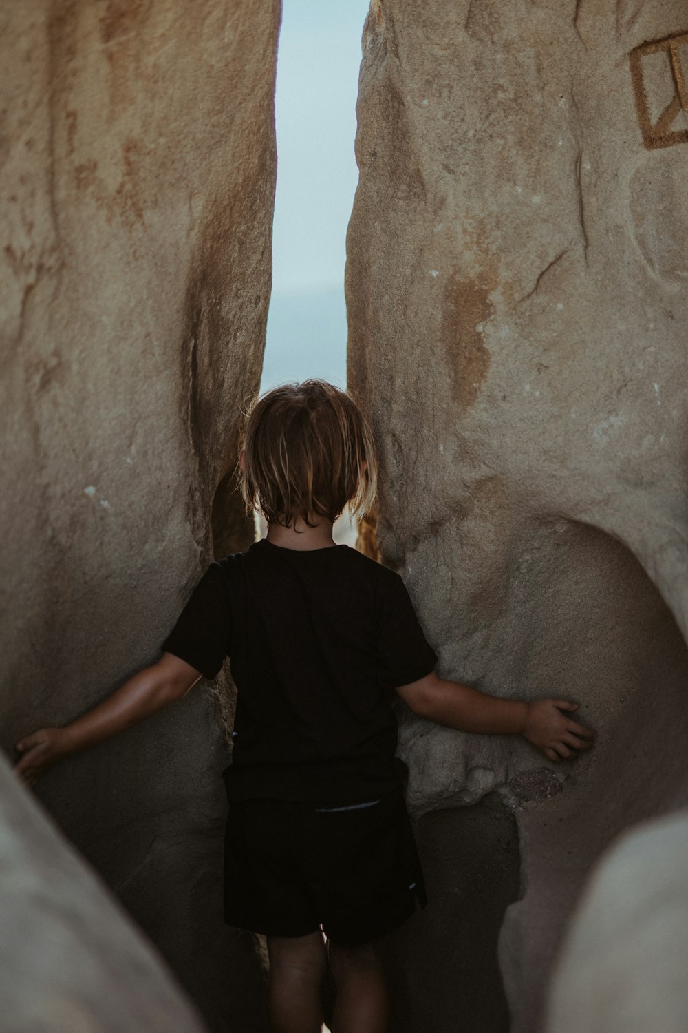 woman in black t-shirt standing beside brown rock formation during daytime