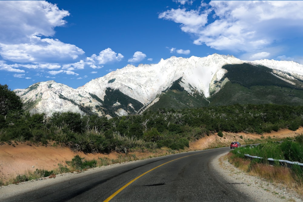 gray concrete road near green grass and snow covered mountain during daytime