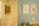 A blurred photograph of a light-colored wall with a hanging sign that reads 'Pedro Samuel' in dark, handwritten letters. The background shows a slightly out-of-focus interior room with a light blue wall and several framed pictures.