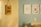 A blurred photograph of a light-colored wall with a hanging sign that reads 'Pedro Samuel' in dark, handwritten letters. The background shows a slightly out-of-focus interior room with a light blue wall and several framed pictures.