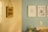 A blurred photograph of a light-colored wall with a hanging sign that reads 'Pedro Samuel' in dark, handwritten letters. The background shows a slightly out-of-focus interior room with a light blue wall and several framed pictures.