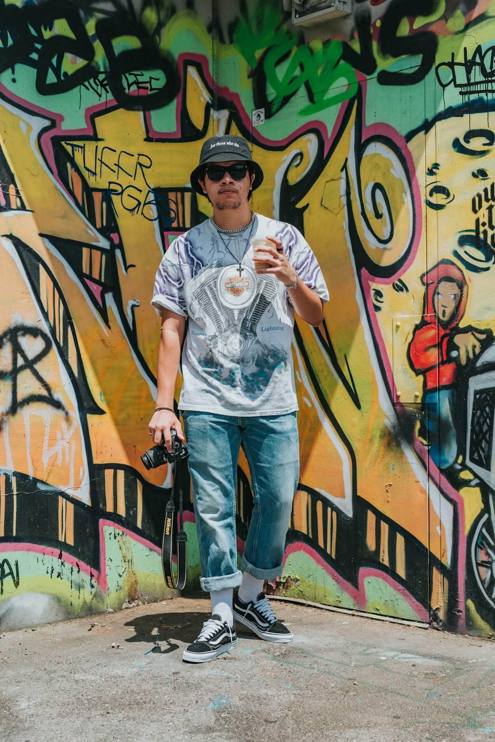 man in white crew neck t-shirt and blue denim jeans standing beside graffiti wall