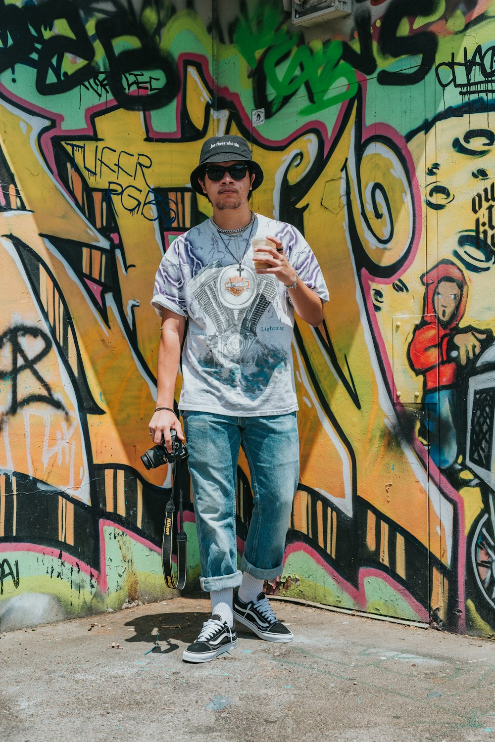 Homme en t-shirt à col rond blanc et jean en denim bleu debout à côté d’un mur de graffitis