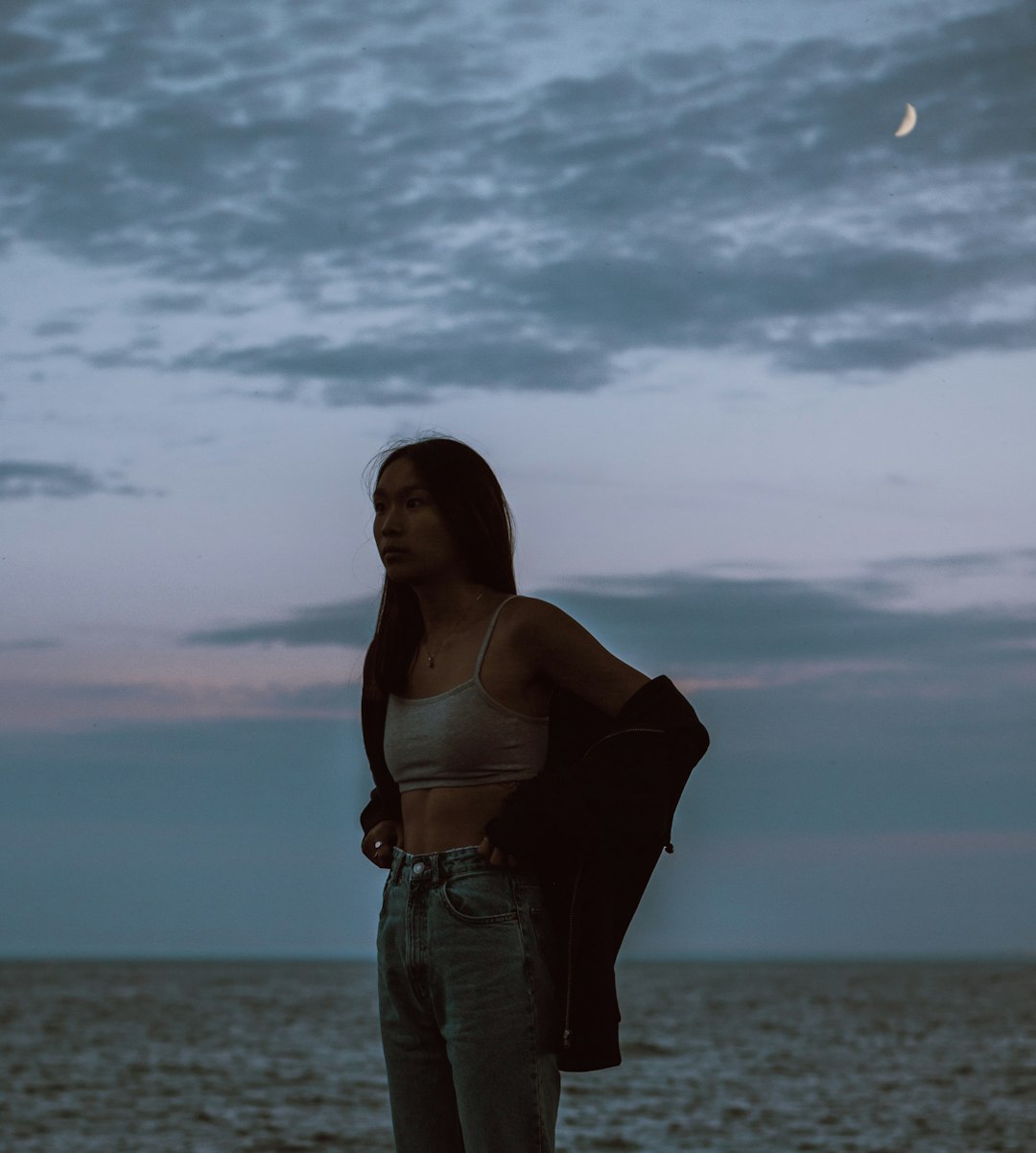 woman in white spaghetti strap top and blue denim shorts standing on beach during daytime