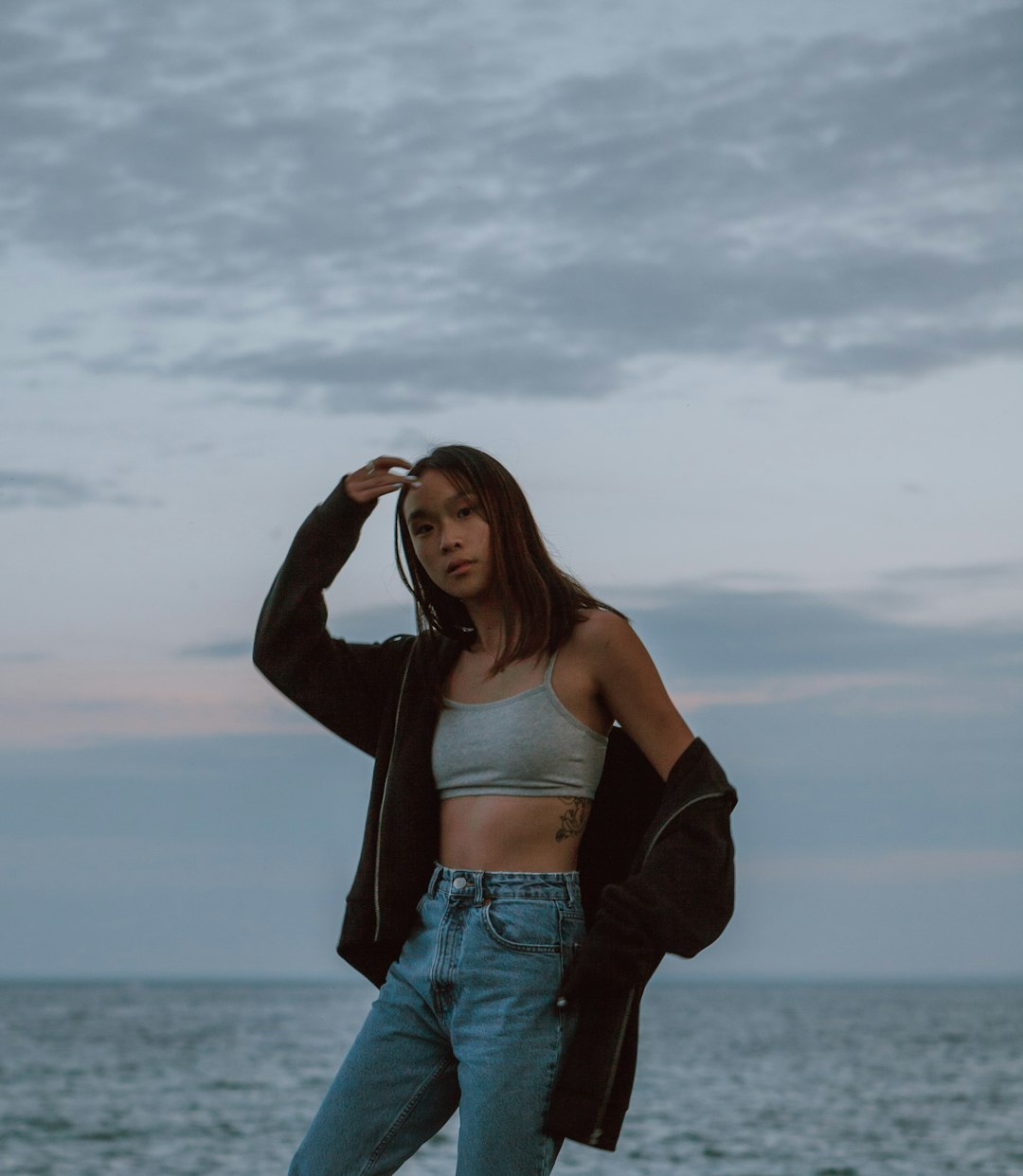 woman in black brassiere and blue denim jeans standing near sea during daytime