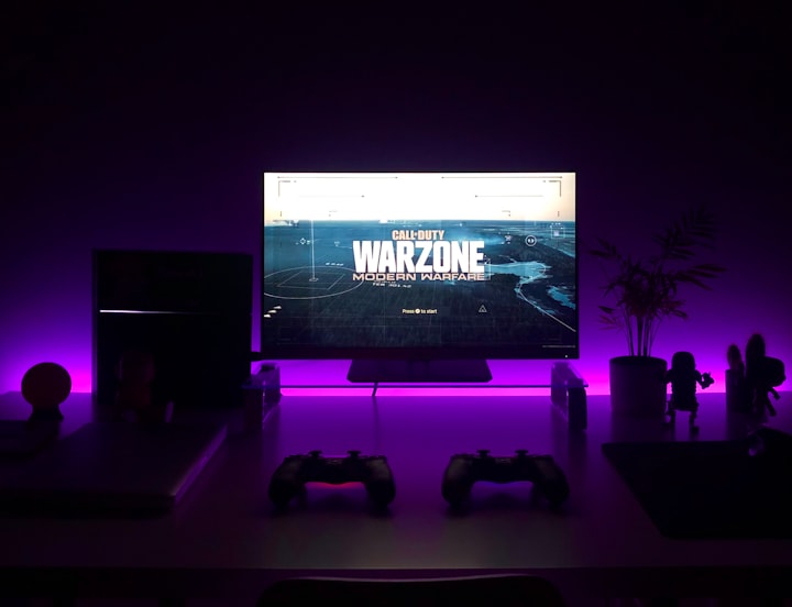 A TV (alongside two PS4 controllers) connected to a gaming console displaying the standby screen for Call of Duty Warzone. 