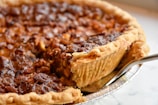 A hand holding a slice of pecan pie with glossy nuts and rich filling.