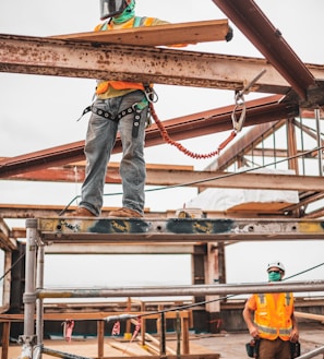 man in blue denim jeans and blue denim jacket standing on orange metal bar during daytime