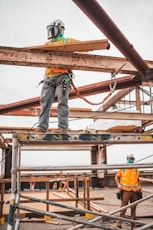 man in blue denim jeans and blue denim jacket standing on orange metal bar during daytime