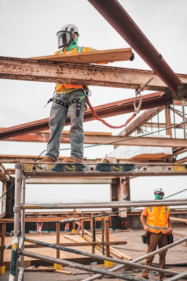 Workers wearing MV Protec Brasil safety gear on a construction site, demonstrating proper use of helmets and harnesses.