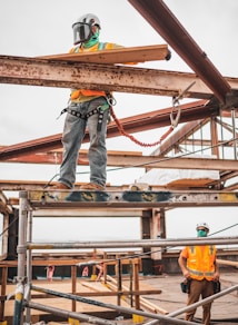 man in blue denim jeans and blue denim jacket standing on orange metal bar during daytime