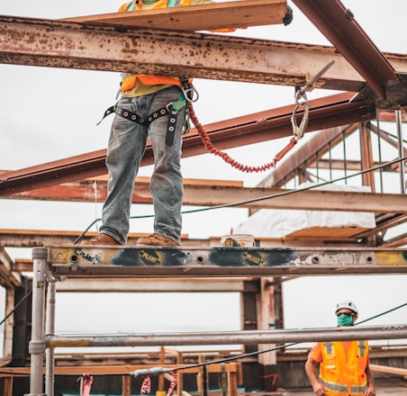 man in blue denim jeans and blue denim jacket standing on orange metal bar during daytime