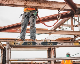 man in blue denim jeans and blue denim jacket standing on orange metal bar during daytime