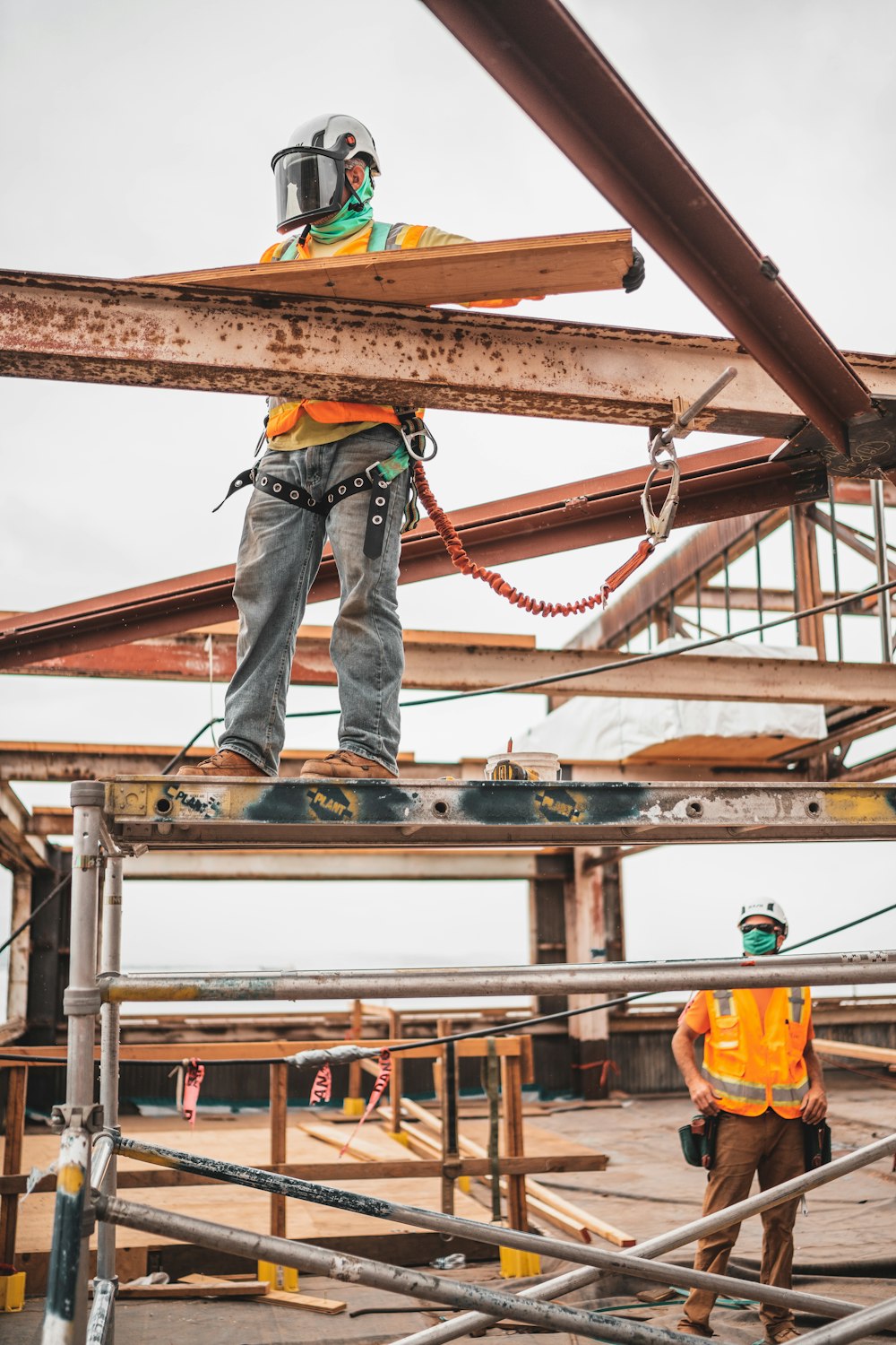 man in blue denim jeans and blue denim jacket standing on orange metal bar during daytime