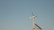 A wind turbine with a solar panel against a clear blue sky, placed on a simple metallic structure. The scene conveys a sense of clean, renewable energy and tranquility.