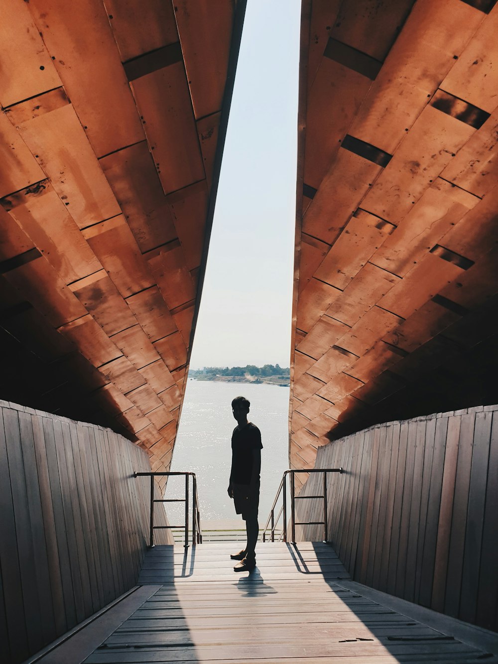 silhouette di un uomo in piedi in un tunnel di legno marrone durante il giorno