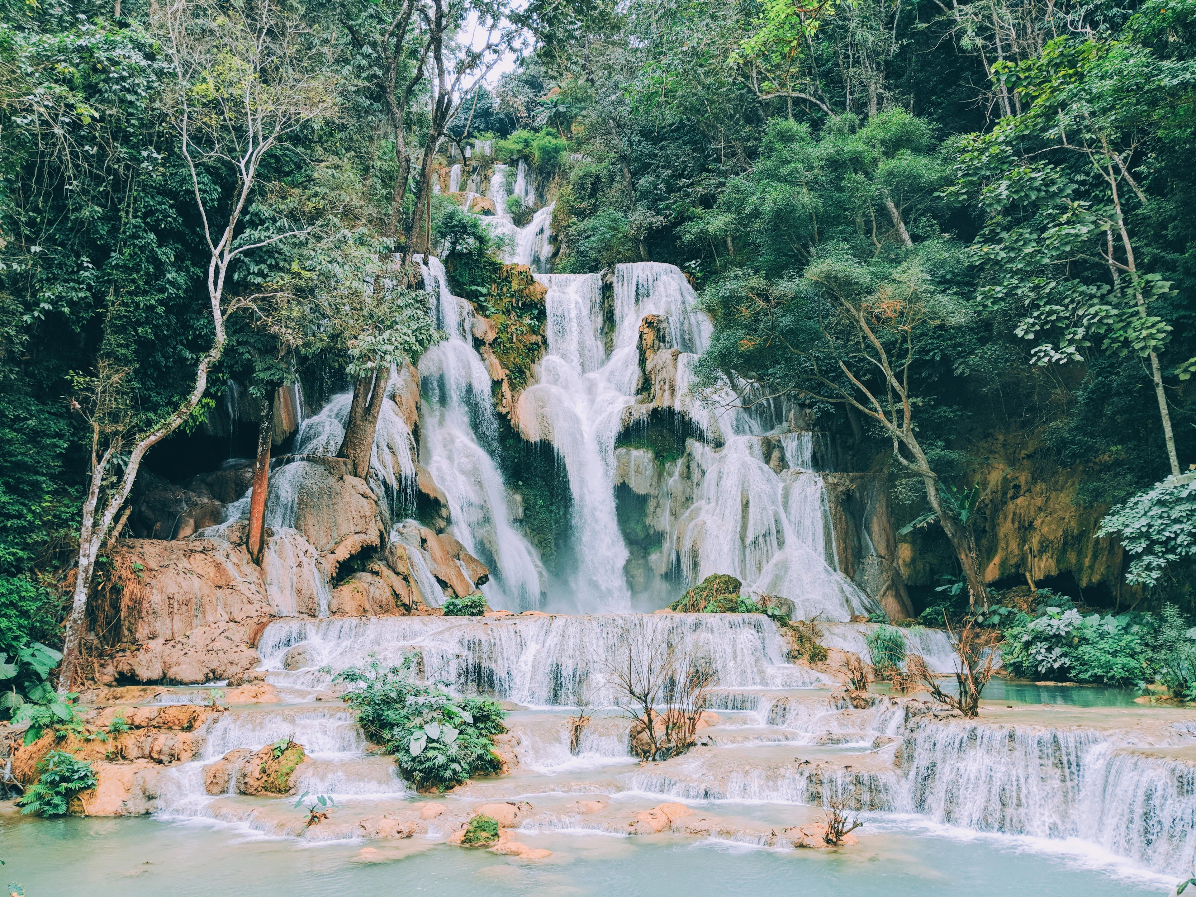 Kuang Si Falls near Luang Prabang, white water spilling down tiers of pale travertine terraces into the milky turquoise pools below, framed by dense green forest