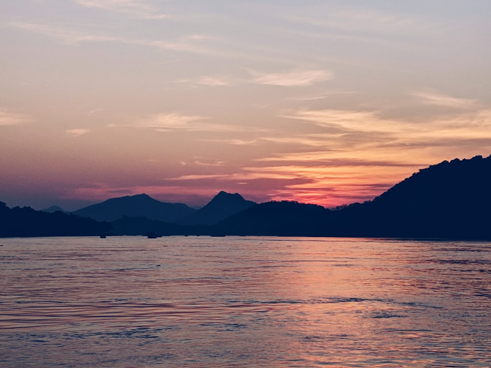 silhouette of mountain near body of water during sunset