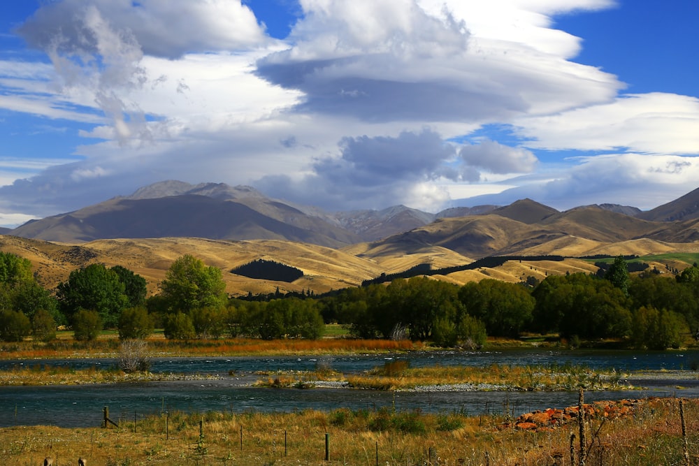 green grass field near mountain under white clouds during daytime