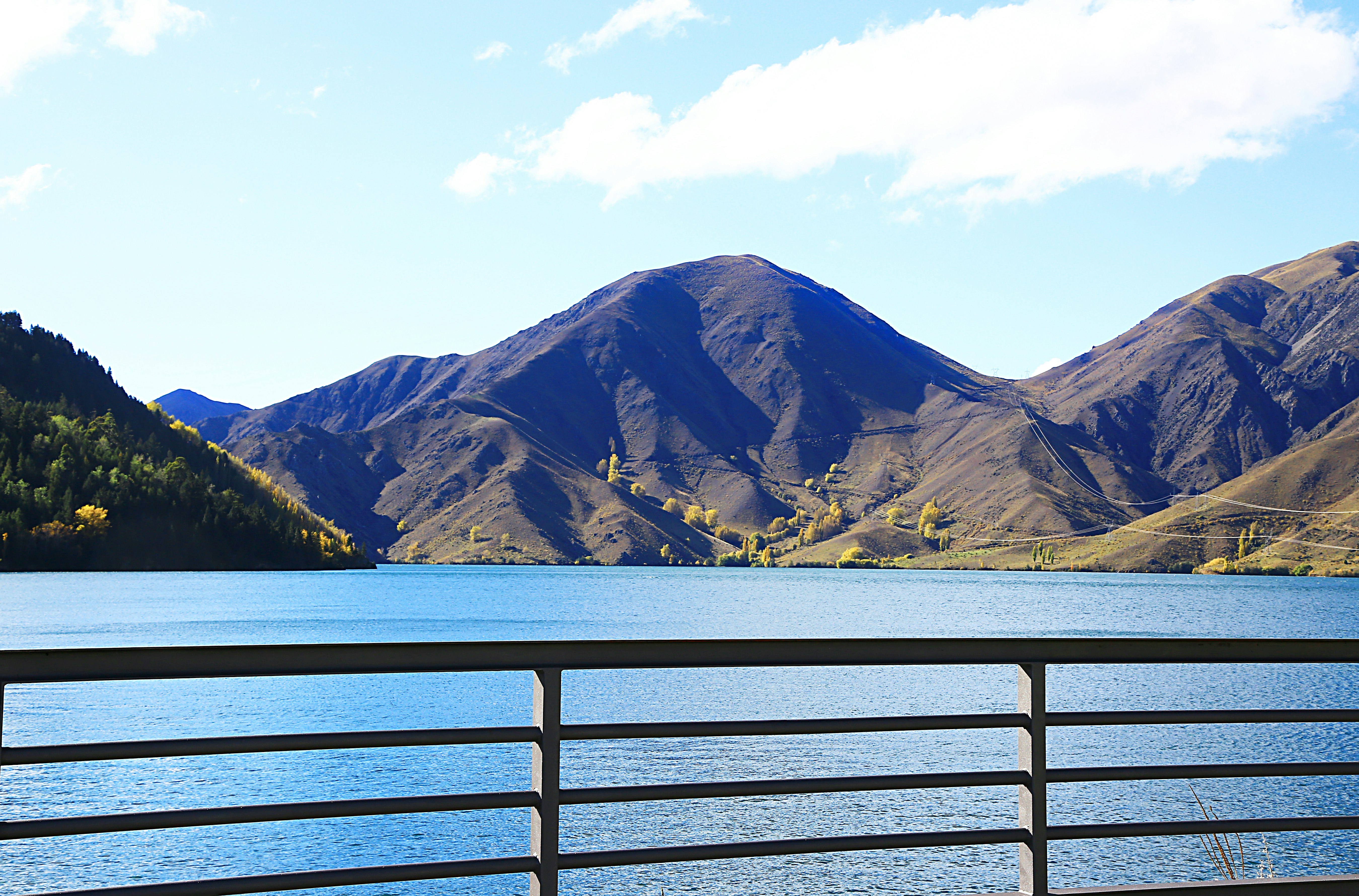 brown wooden fence near body of water and mountain during daytime