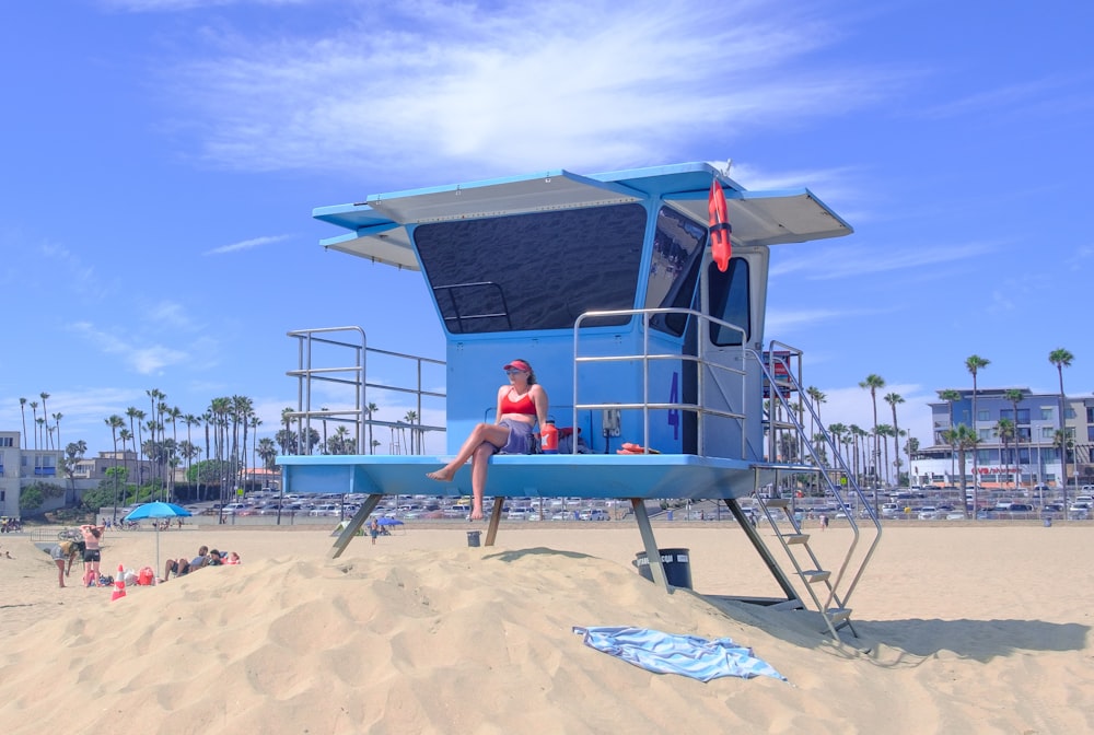 woman in red bikini sitting on blue and white boat on beach during daytime